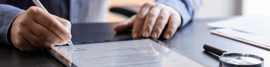 A man at a desk in an office signing an einvoice on a tablet device with a stylus pen.