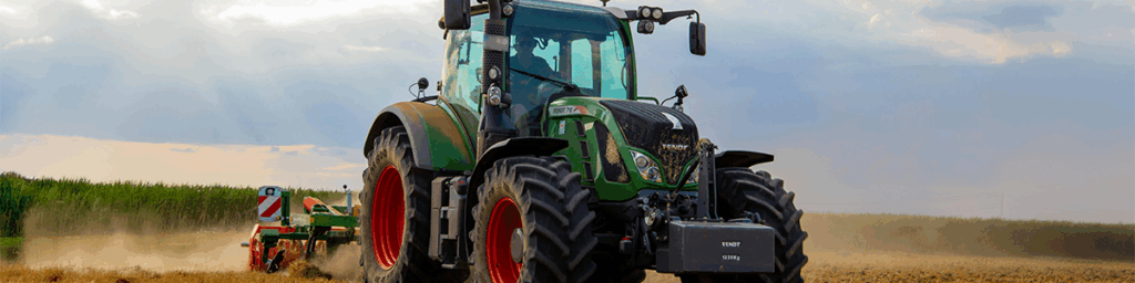 A green tractor plowing in a field with blue skies.